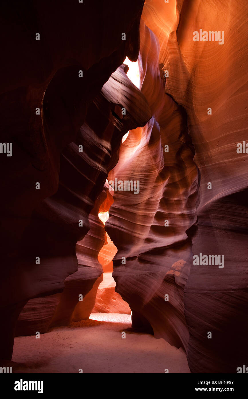 Bright sunlight streaming into steep curving red rock walls of Antelope Canyon, natural smooth rock formations from water erosion Arizona USA Stock Photo