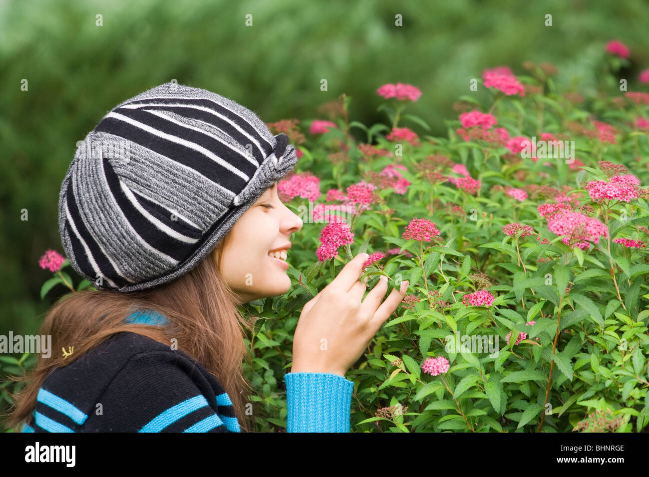 Beautiful woman with hat smelling purple flowers in a garden Stock