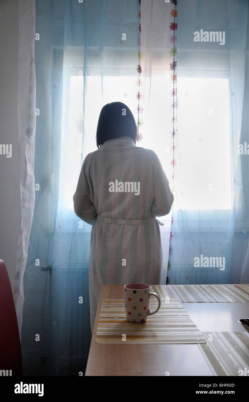 Woman wearing bathrobe standing by window Stock Photo