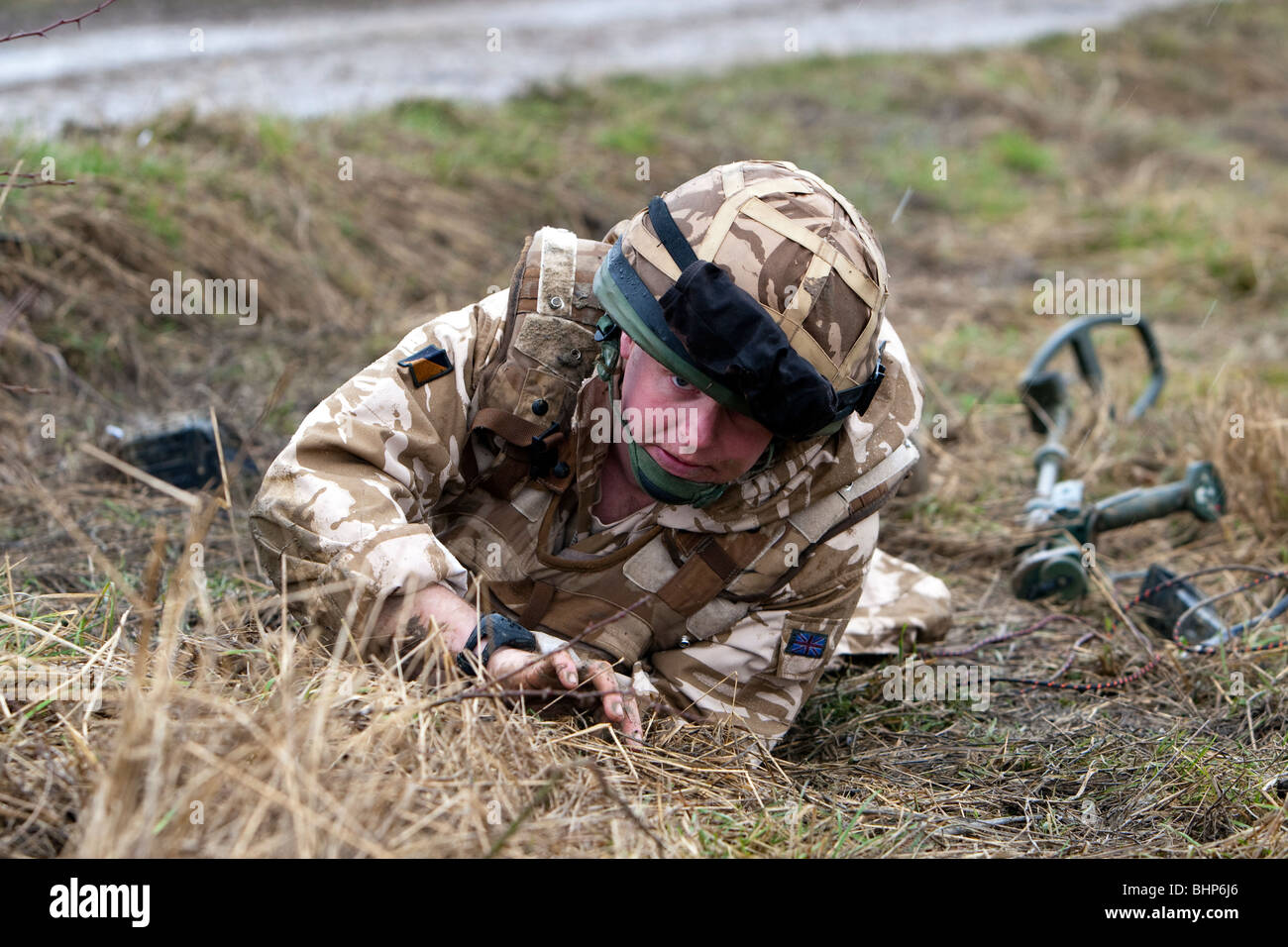 A british soldier uses a metal detector to locate an IED roadside bomb and prepares to destroy it during a training exercise Stock Photo