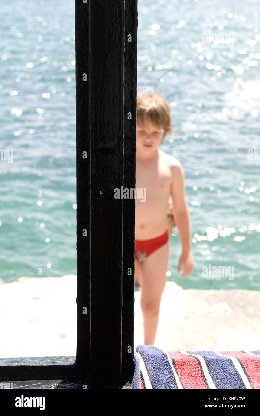 7 year old young boy framed by a winodw stands on jetty with his back to the sea in fowey, cornwall, uk Stock Photo