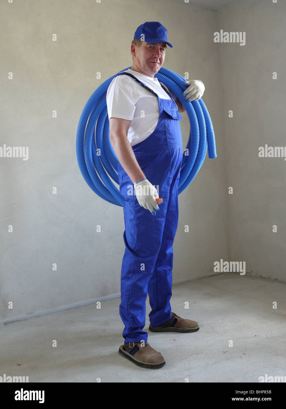 Electrician wearing white shirt, blue cap and blue uniform posing with coil of PVC flexible corrugated cable protection pipe Stock Photo