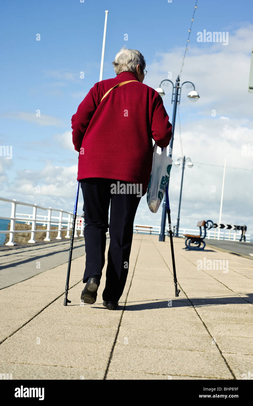Elderly woman walking with the help of two walking sticks, Aberystwyth, Ceredigion, West Wales UK Stock Photo