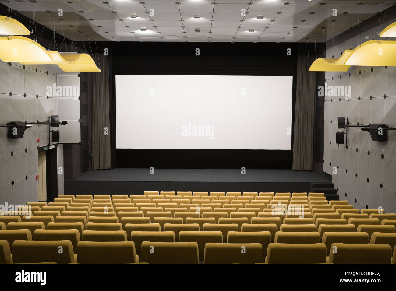 Empty cinema auditorium with line of yellow chairs, stage and projection screen. Ready for adding your own picture. Stock Photo