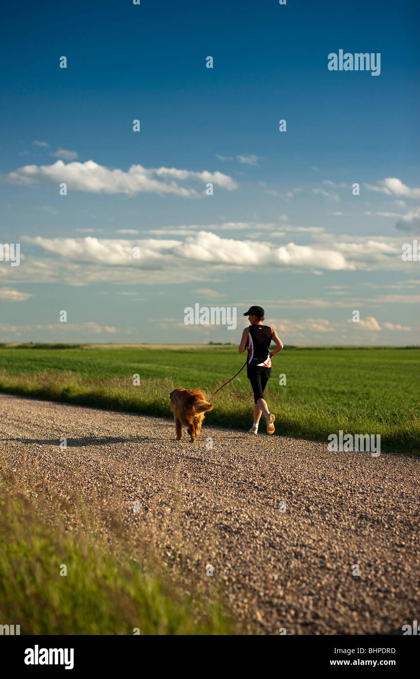 Female Runner And Dog, On Rural Road, Saskatchewan Stock Photo