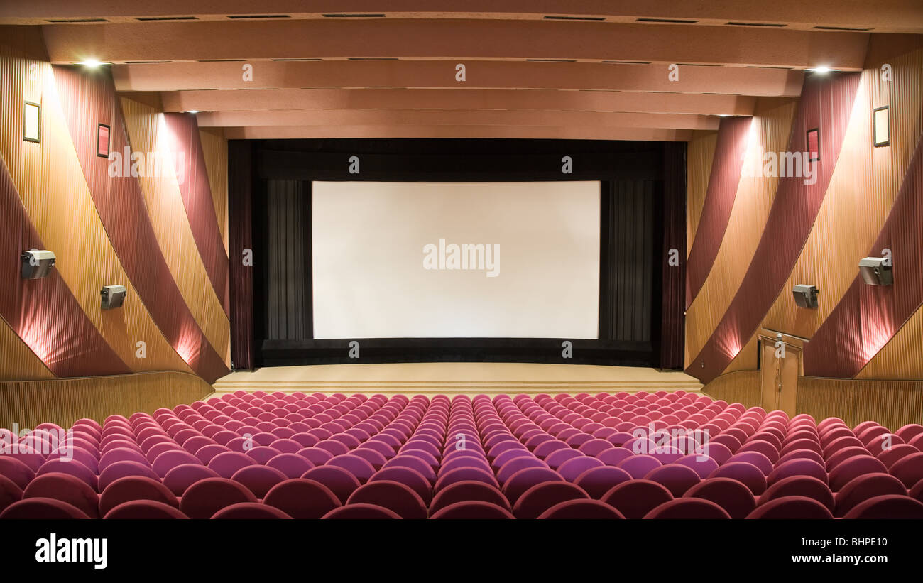 Empty cinema auditorium with line of pink chairs and projection screen. Ready for adding your own picture. Stock Photo