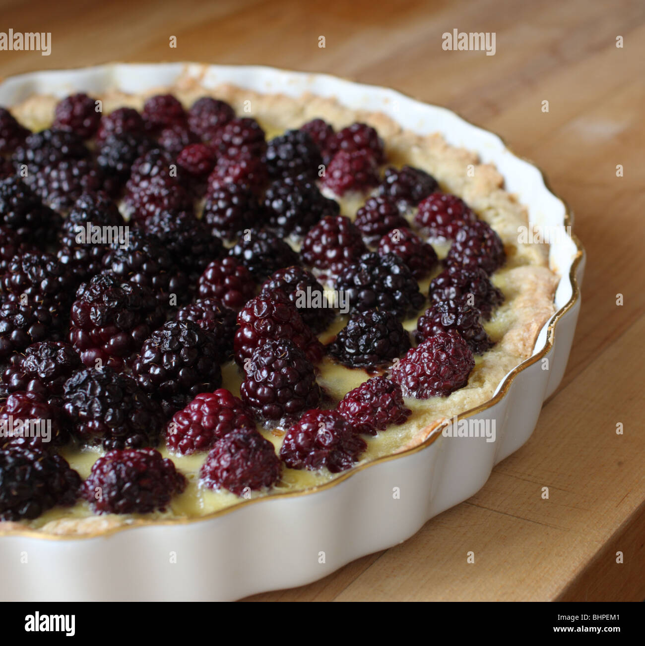 Blackberry tart in a gilt china tart dish on a wooden chopping board Stock Photo