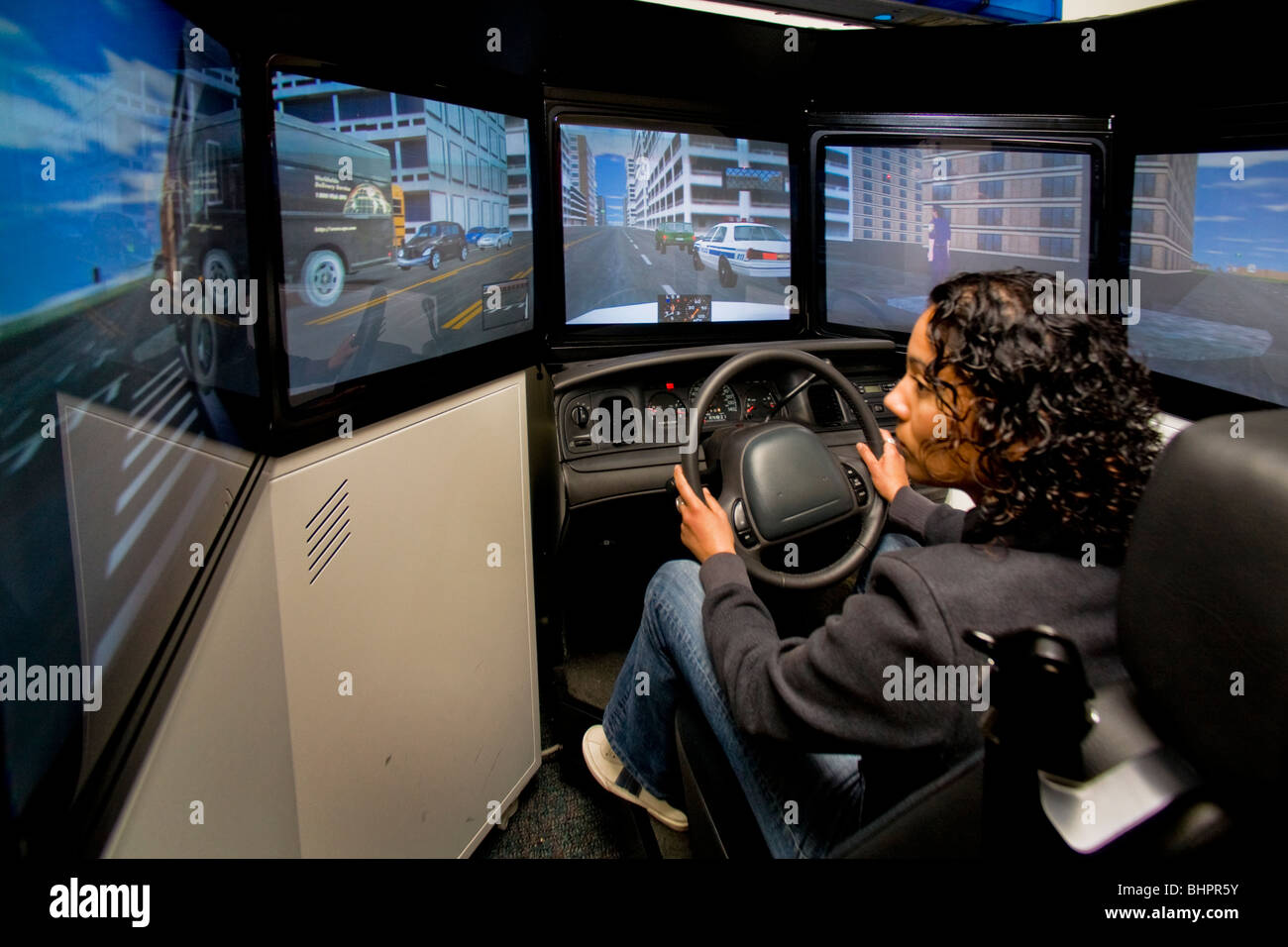 A woman police officer practices high speed driving skills in a patrol car simulator with a real steering wheel and seat. Stock Photo