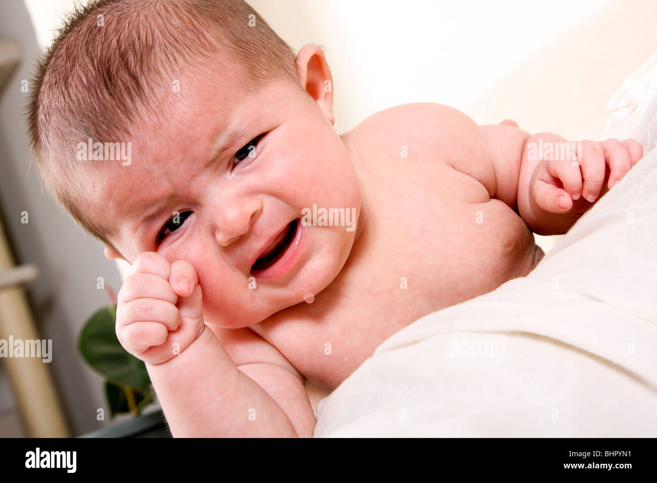 Face of an unhappy unisex Caucasian Hispanic baby crying with tears while rubbing eye. Stock Photo