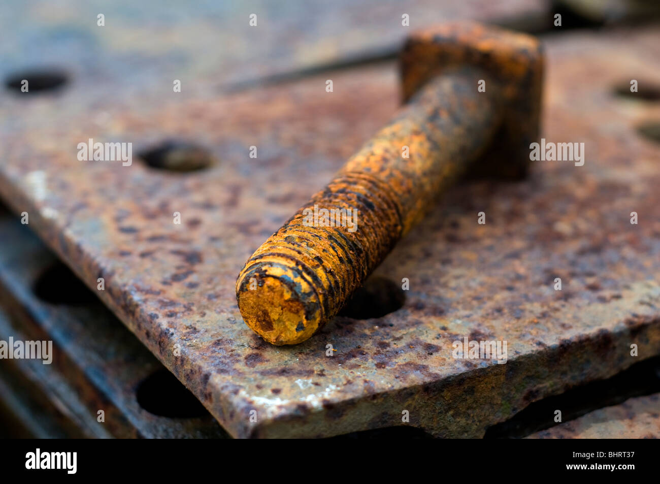 A rusty threaded bolt on a pile of rusting metal plates Stock Photo