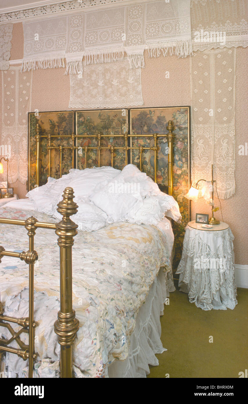 Lace covered wall behind decoupage screen and antique brass bed in