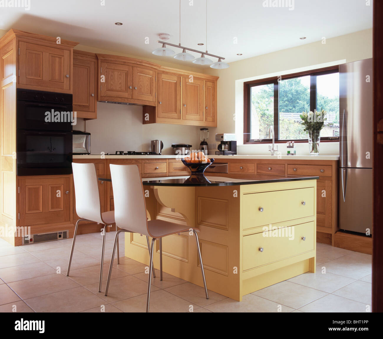 Chairs at breakfast bar on pale yellow island unit in modern kitchen ...