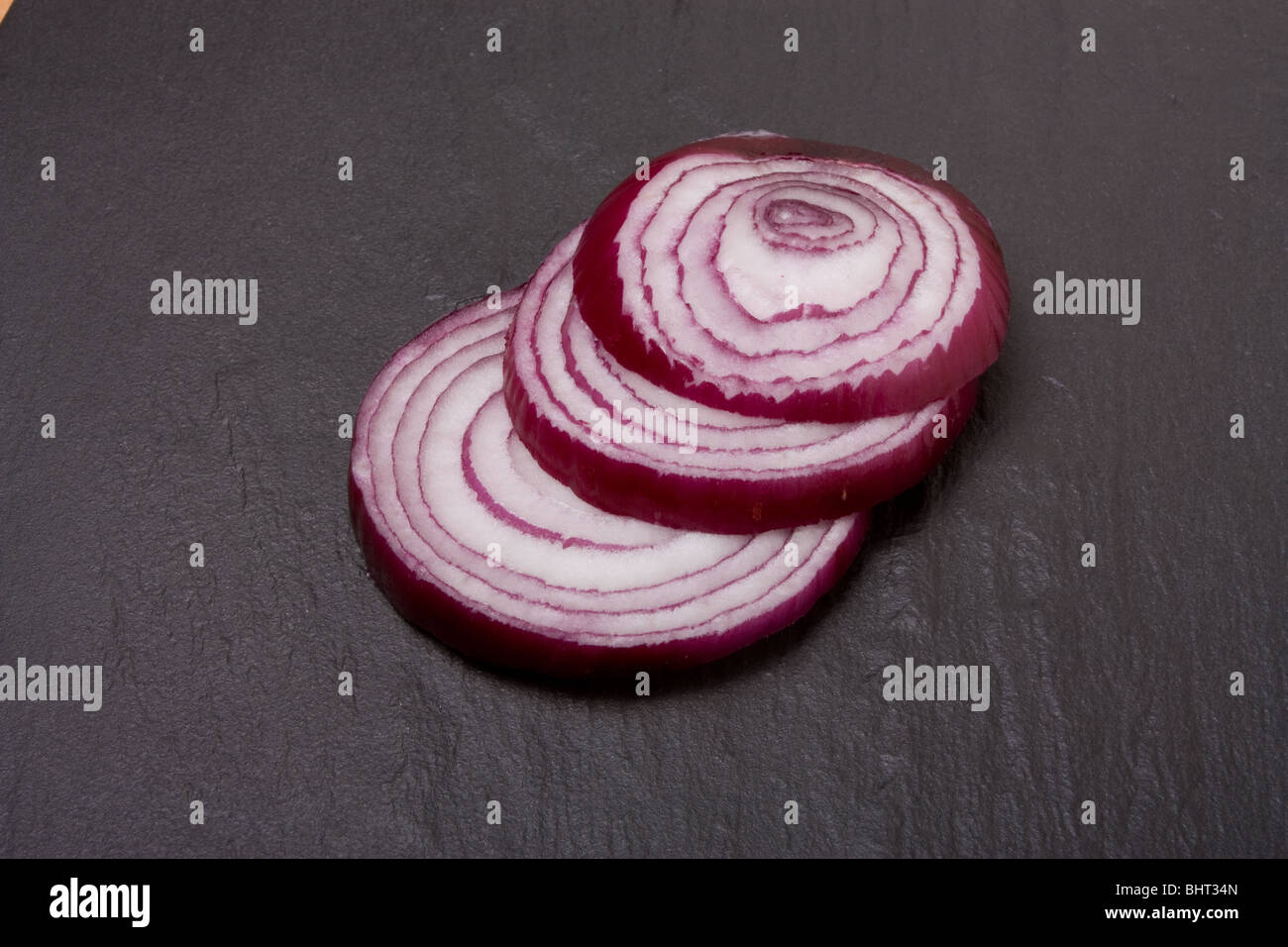 Stepped arrangement of sliced red onion on dark slate background. Stock Photo