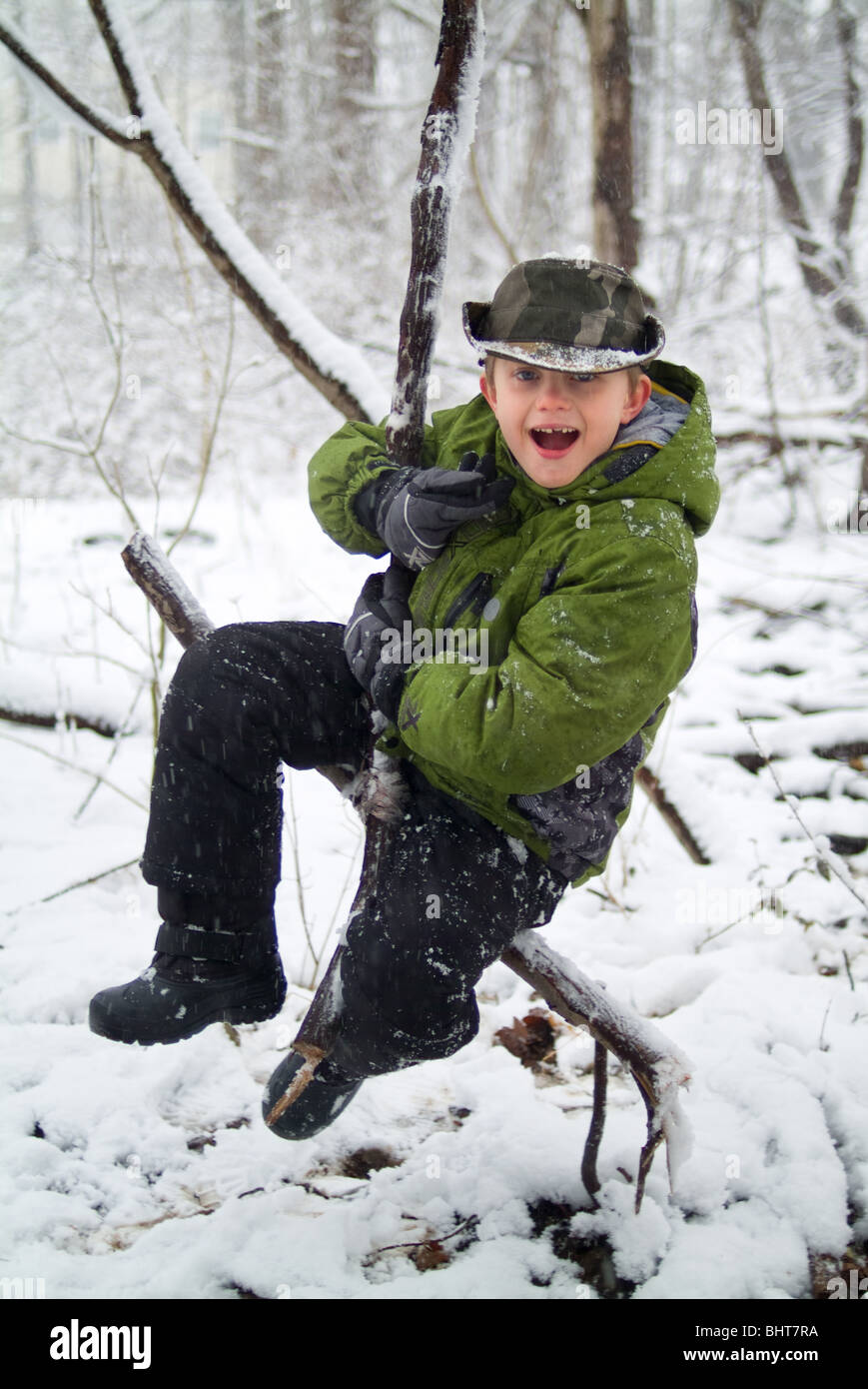 Child playing in woods swinging on a vine in the snow Stock Photo