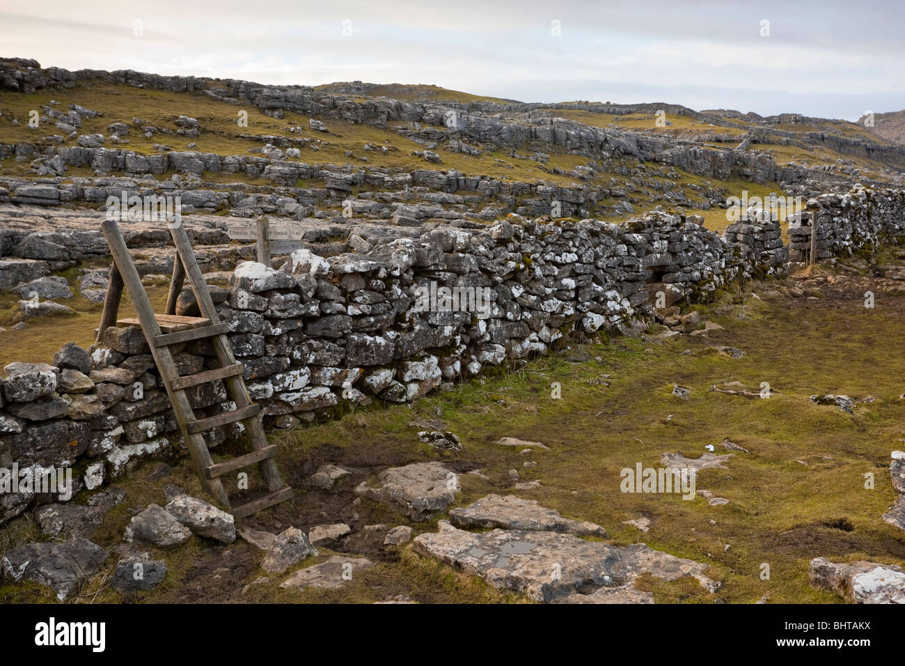 A wooden stile over a stone wall in the Yorkshire dales adjacent to a sign for the Pennine way at Malham Cove Stock Photo