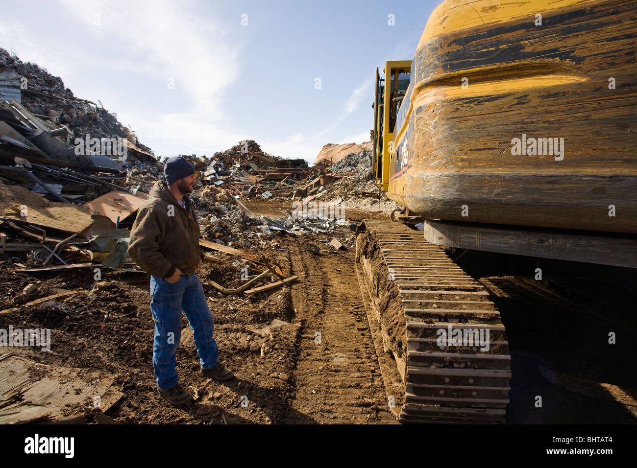 Man standing by excavating machine at scrap metal yard Stock Photo - Alamy