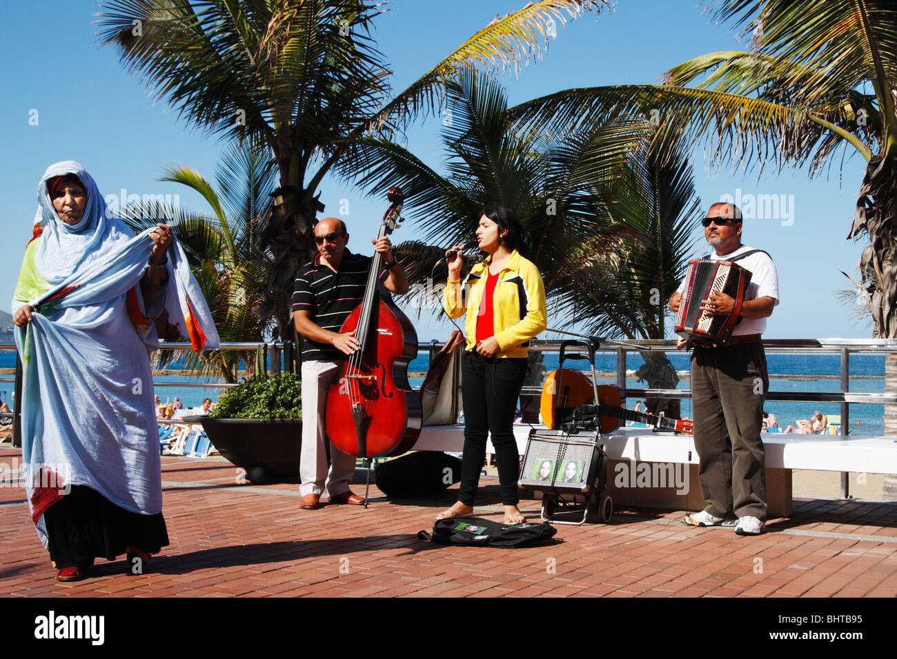 Group of Spanish gypsy musicians busking near Las Canteras beach in Las Palmas, Gran Canaria. North African woman walking past. Stock Photo