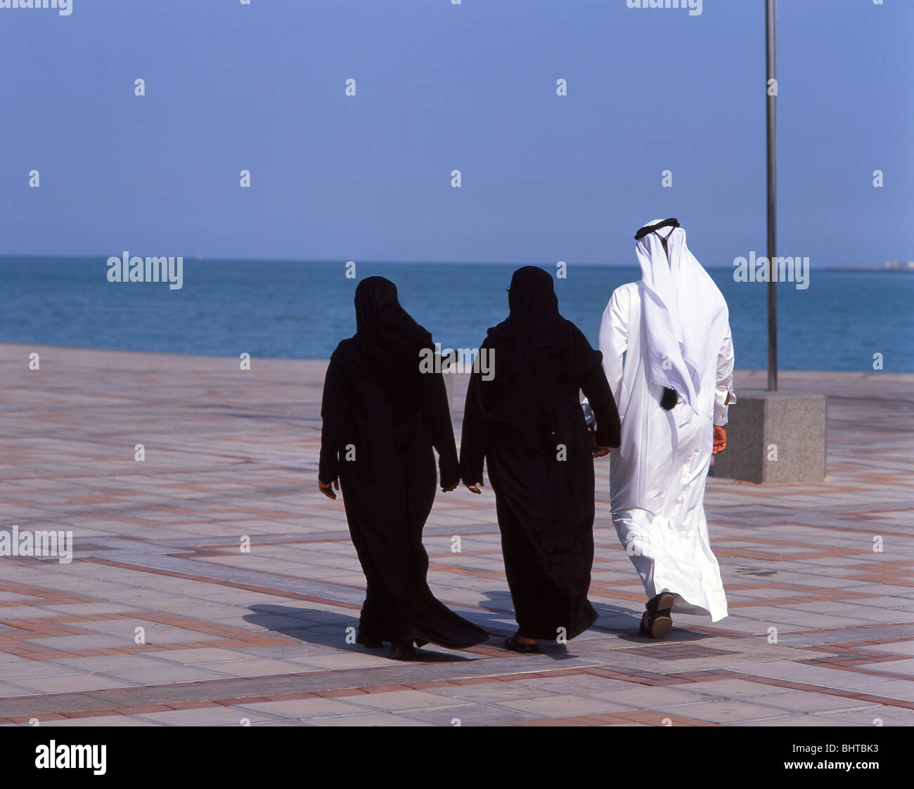 Man and women walking on The Doha Corniche, Doha, Ad Dawhah Municipality, State of Qatar Stock Photo