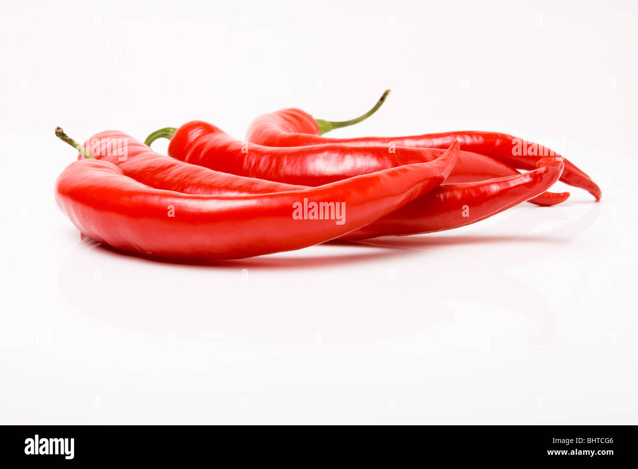 Four vibrant red chillis on a backdrop of dark slate. Stock Photo