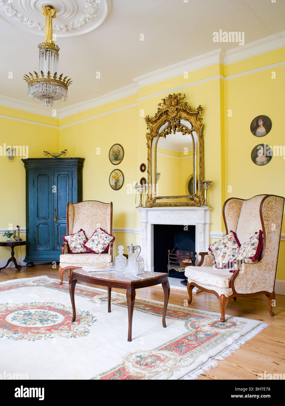Ornate gilt antique mirror above fireplace in yellow drawing room with ...