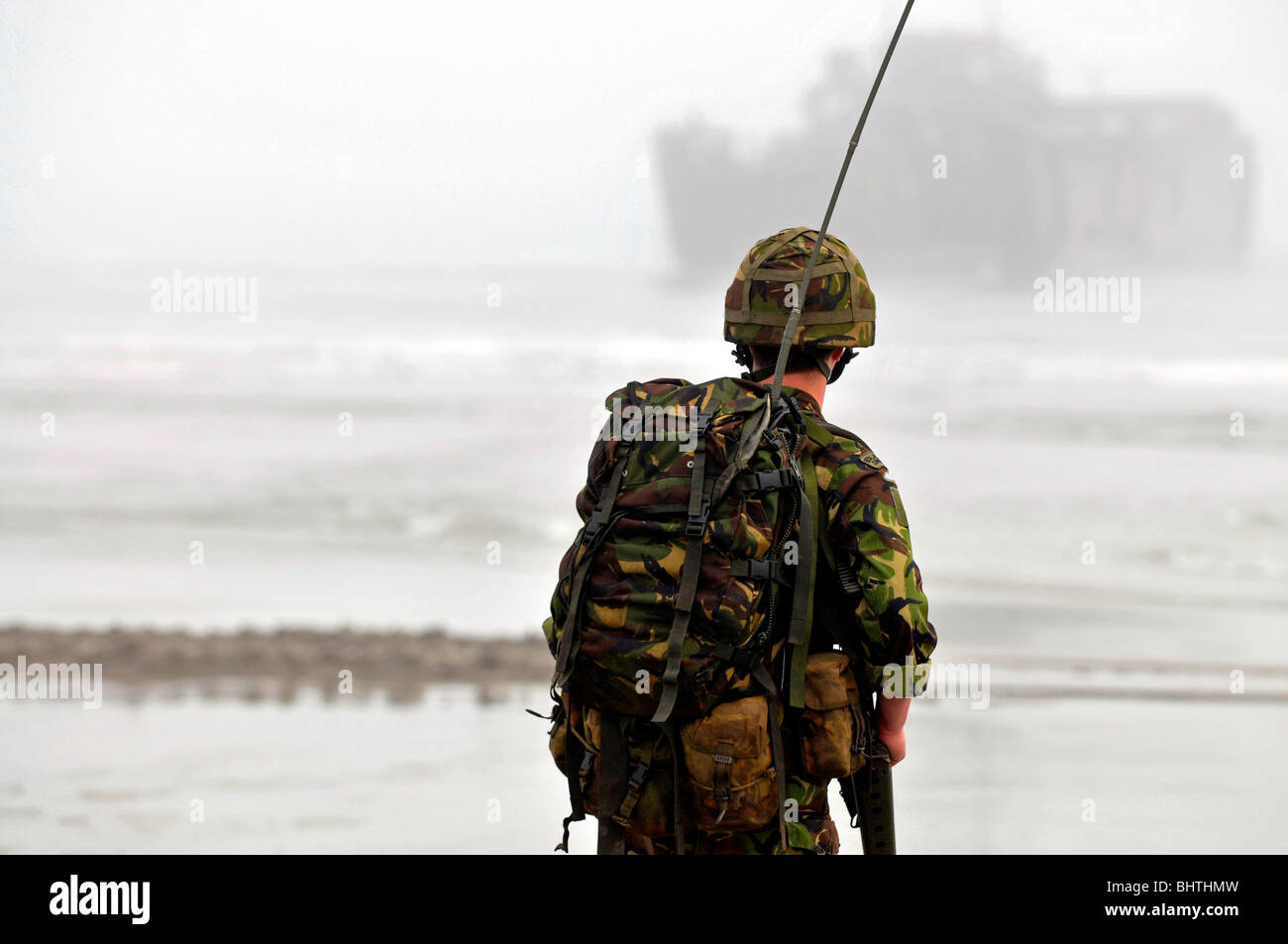Communications Marine with landing craft behind, soldier with communications radio during a beach landing, UK Stock Photo