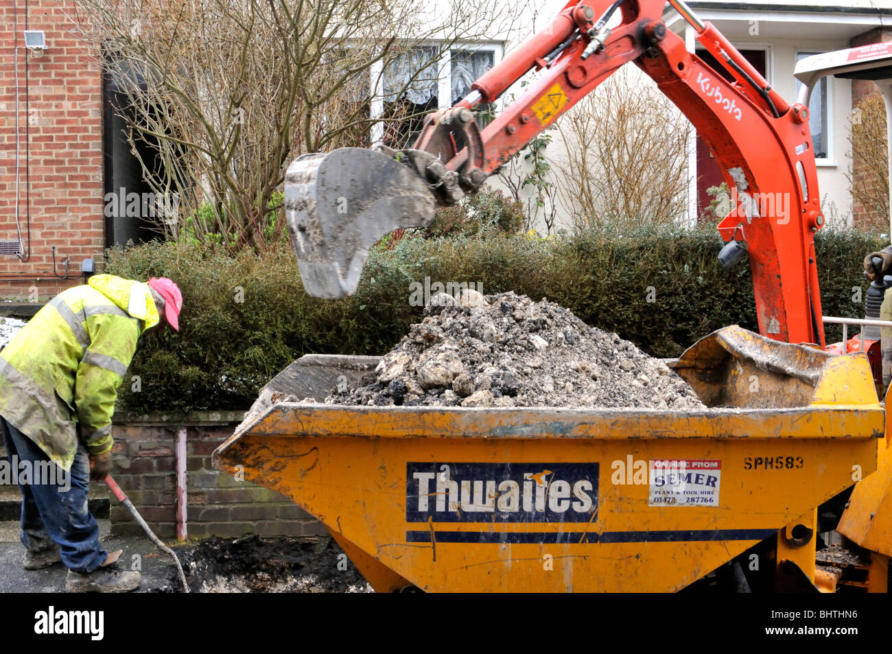 Mini digger at work digging up the pavement to replace gas pipe, UK