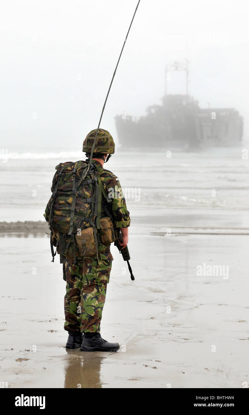Communications Marine with landing craft behind, soldier with communications radio during a beach landing, UK Stock Photo