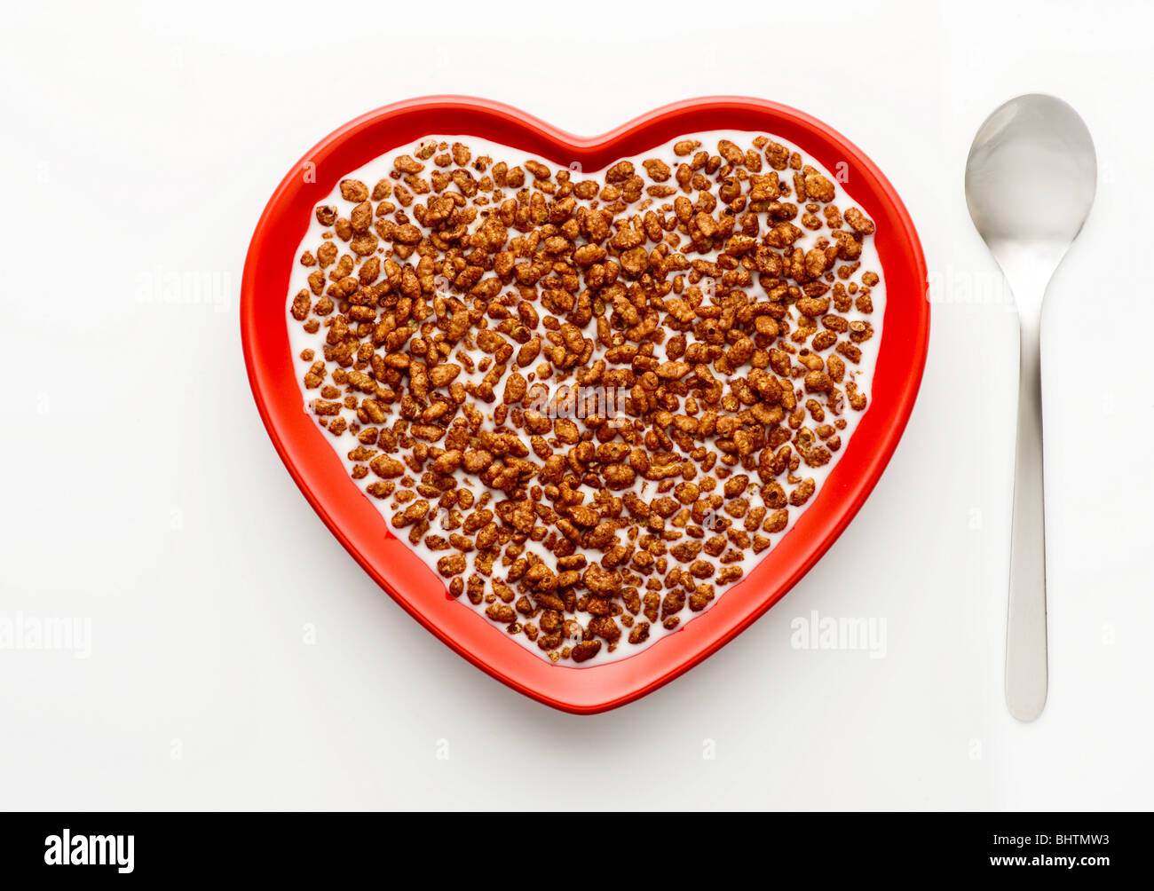 Studio shot of red heart shaped bowl of coco pops and milk with a spoon,on a white background, shot from above. Stock Photo