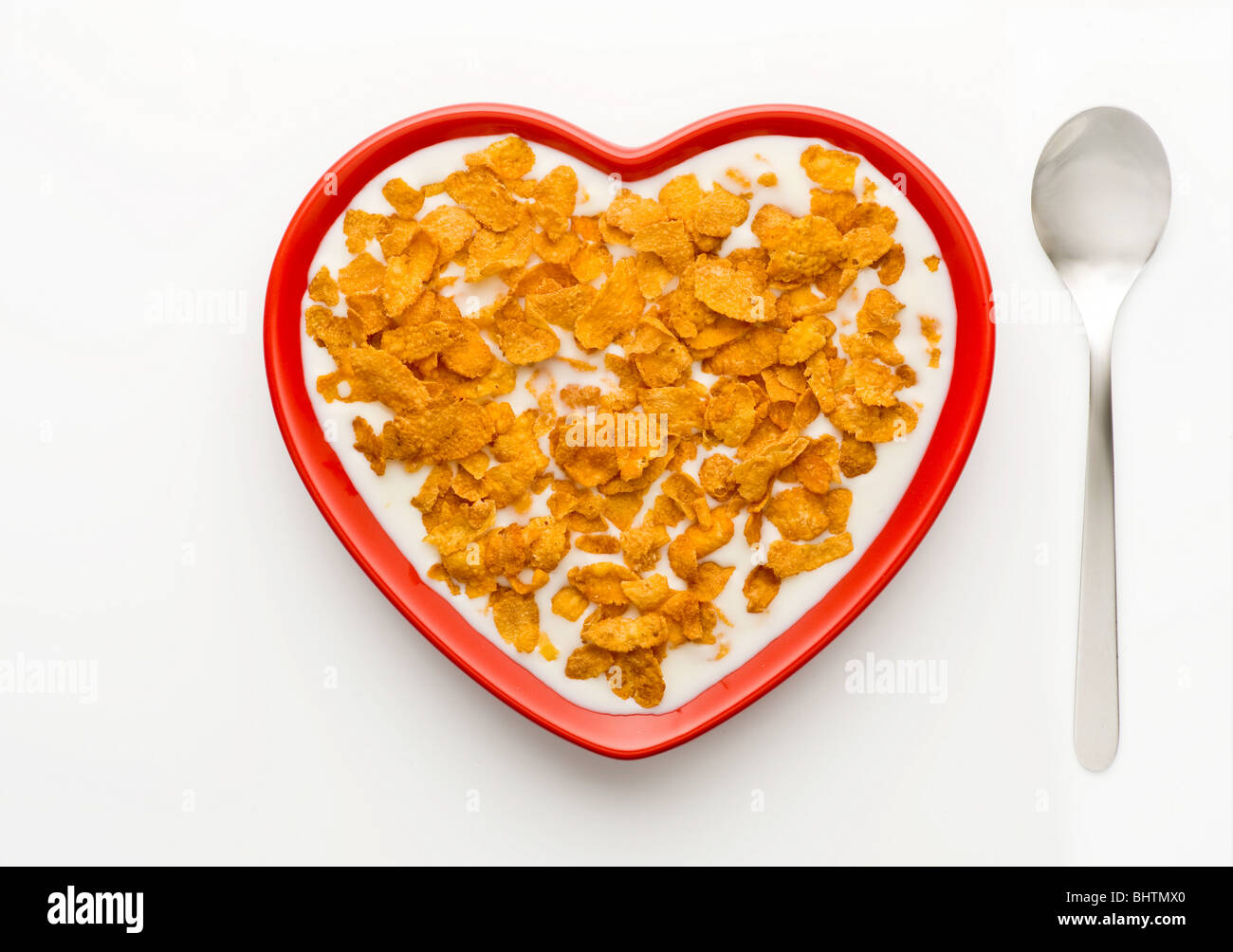 Studio shot of red heart shaped bowl of corn flakes and milk on a white background, shot from above. Stock Photo
