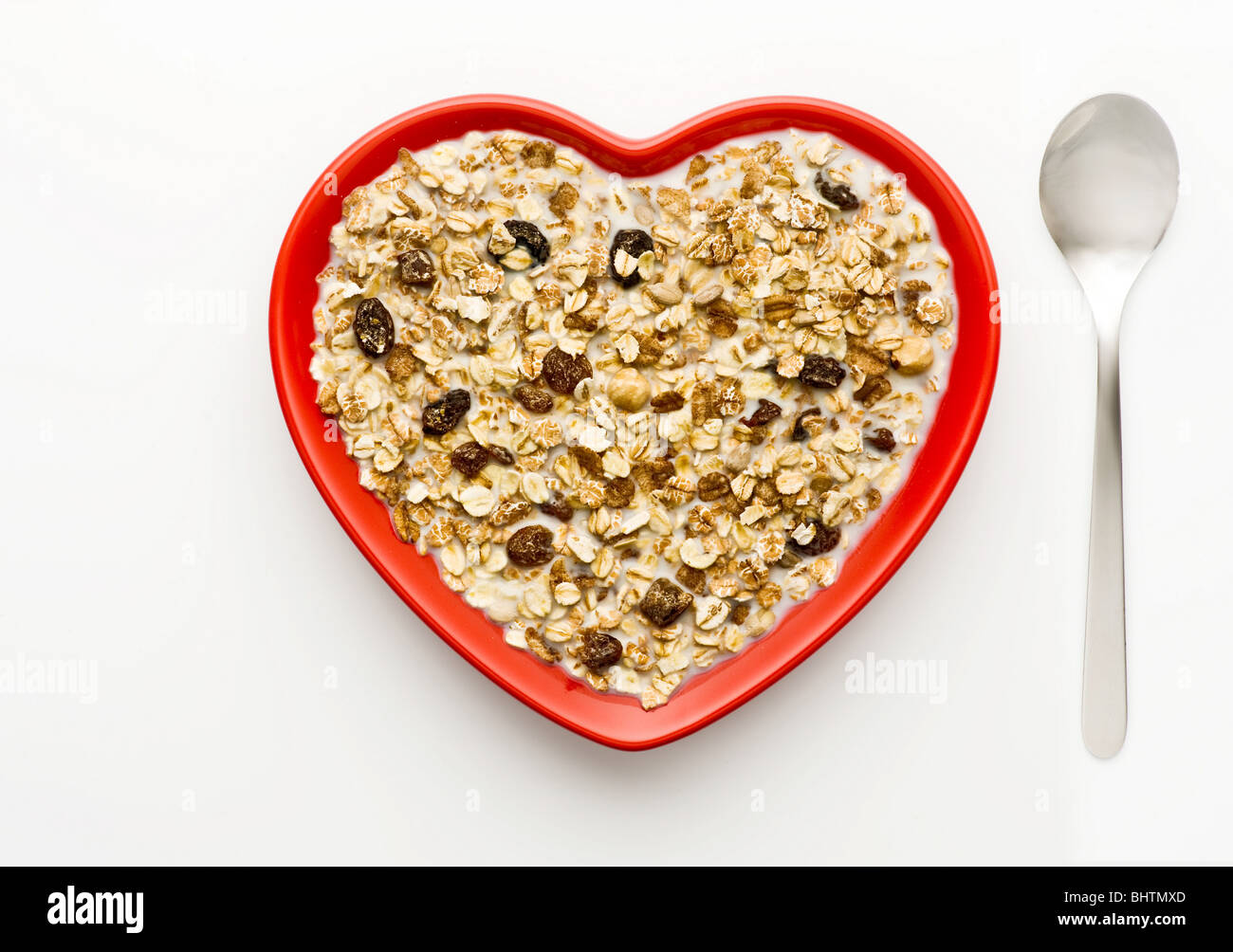 Studio shot of red heart shaped bowl of muesli and milk on a white background, shot from above. Stock Photo