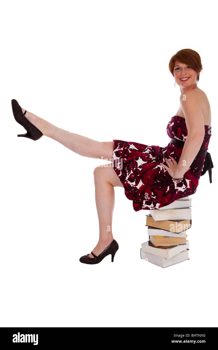 Young women is sitting on thick books with leg in the air. Smiling on white background Stock Photo