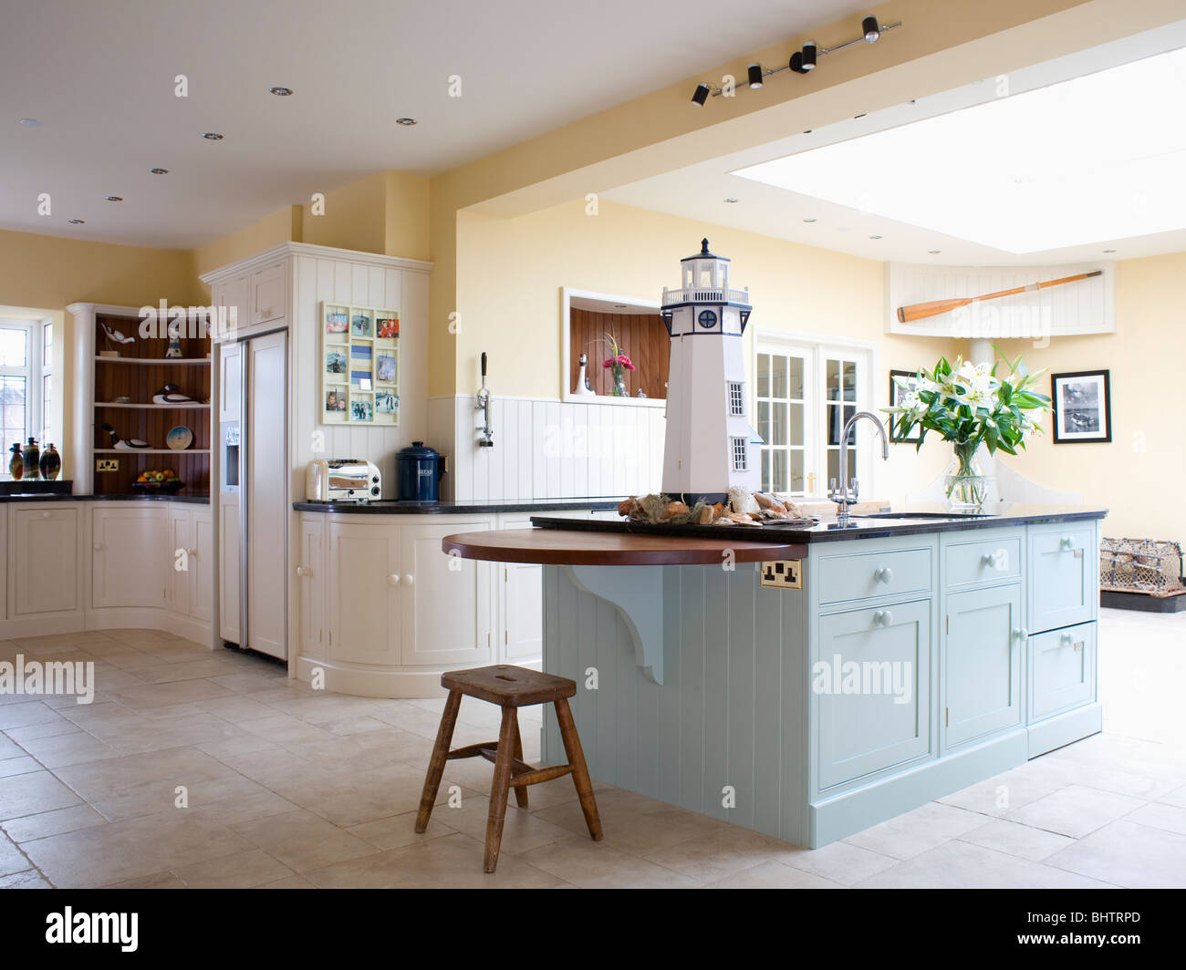 Pastel blue island unit in large pale yellow kitchen extension with fitted cream units and limestone flooring Stock Photo