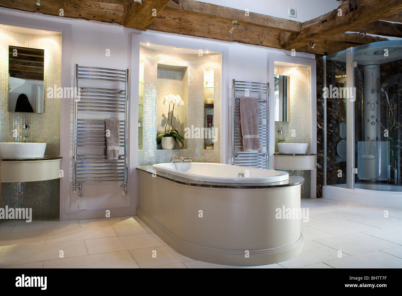 Basins in lighted alcoves in large modern bathroom with bath extending