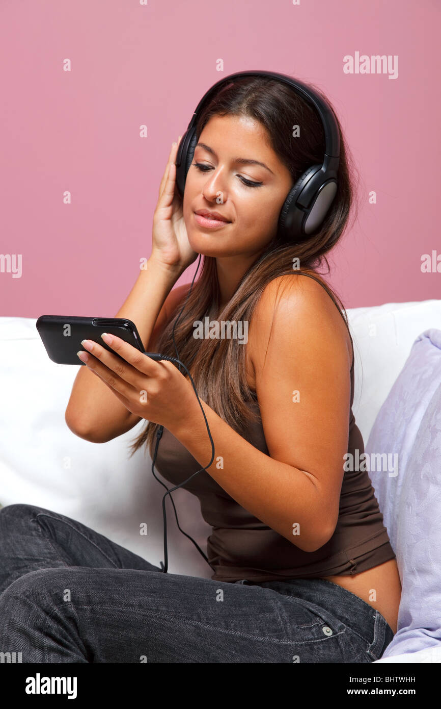 Woman sat in an armchair wearing headphones listening to a music video on her mp3 player Stock Photo