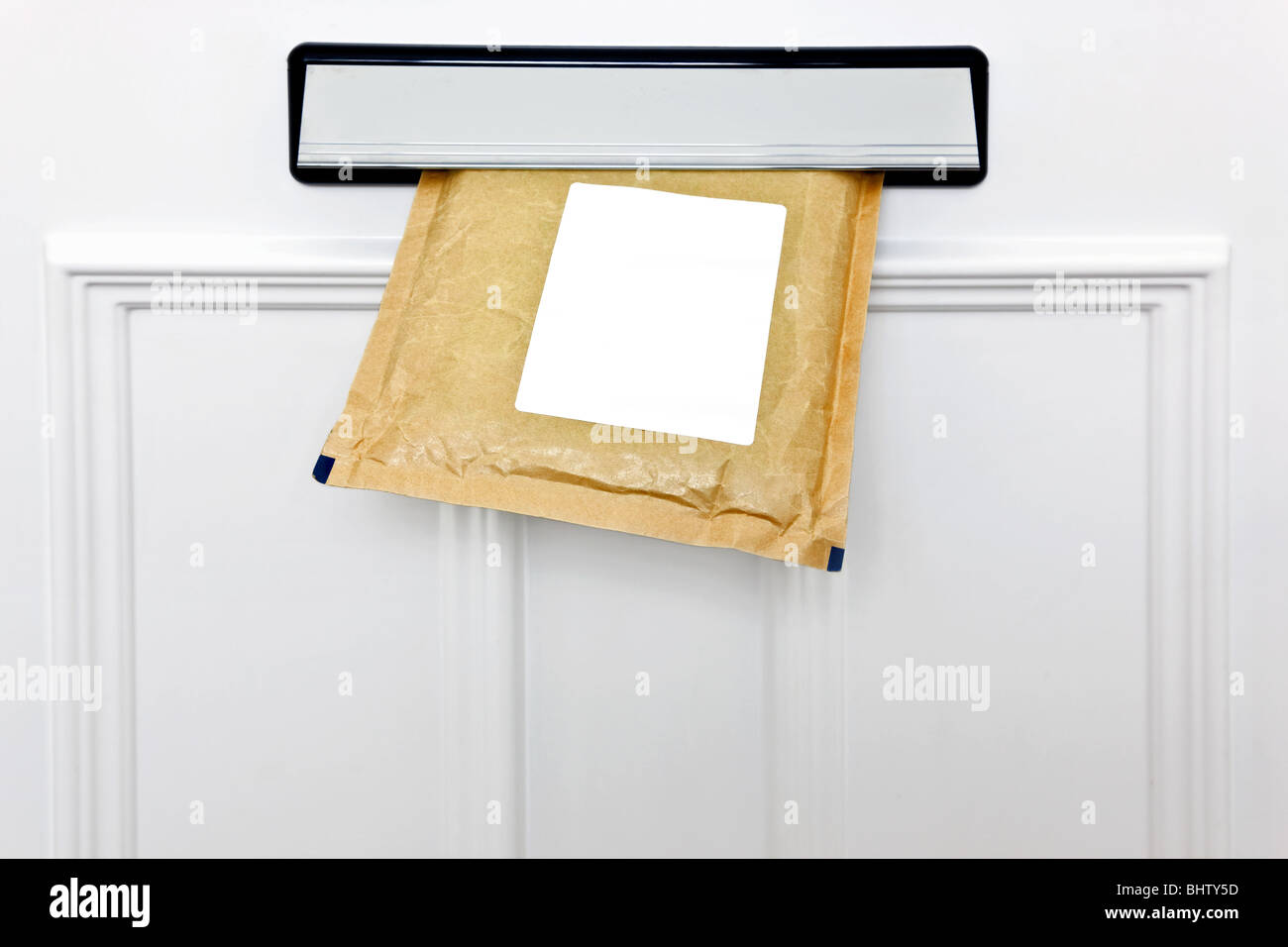 A padded envelope in the letterbox of a white front door, blank label for you to add your own name and address. Stock Photo