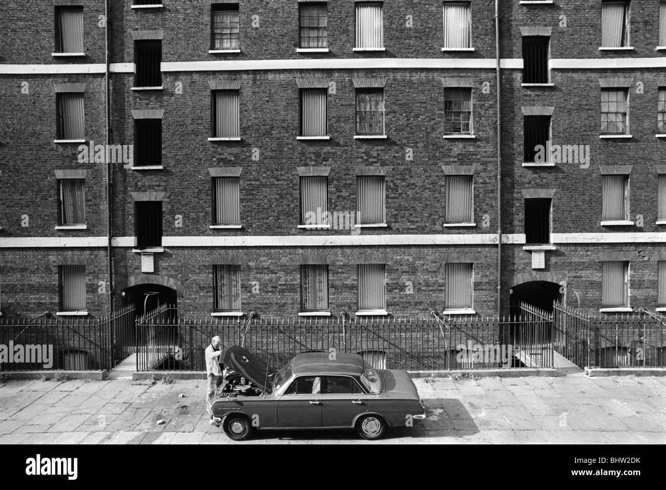 Victorian tenement slums, Peabody Housing Estate. Tower Hamlets Whitechapel east London UK 1970s. Working class man working on his car in front of his housing block.1975 HOMER SYKES Stock Photo