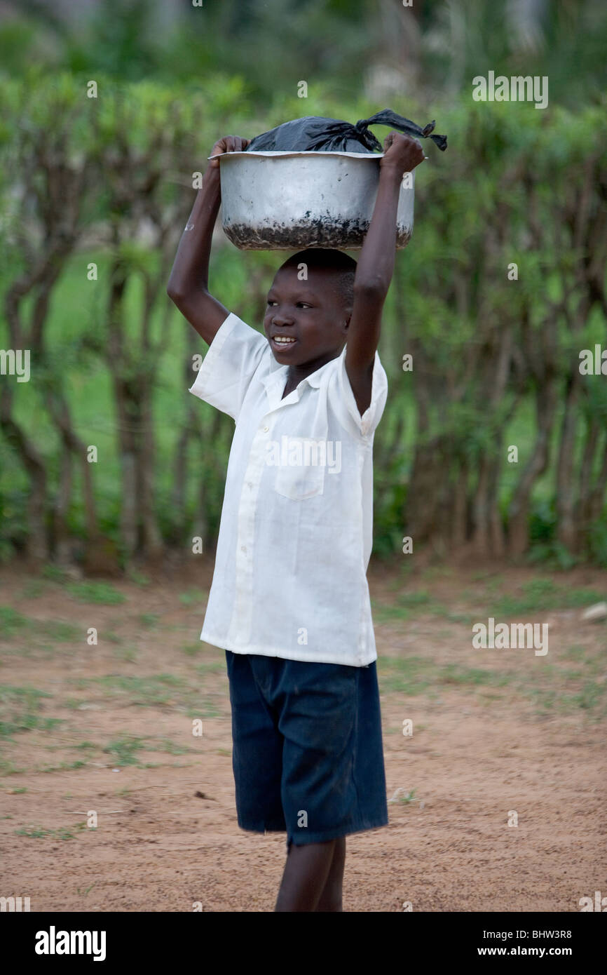 Child carrying tin bowl on his head in Uganda, Africa Stock Photo