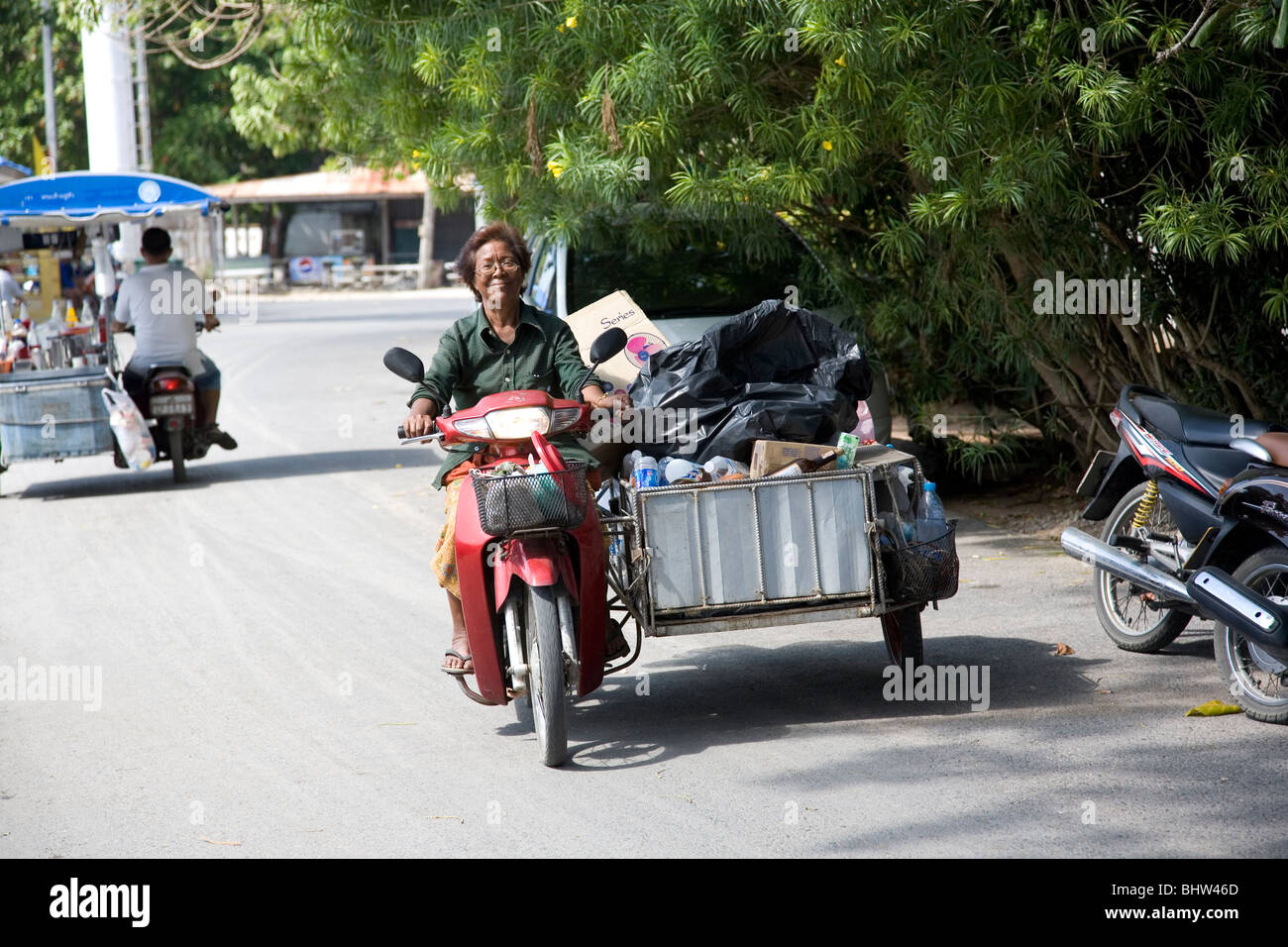 Woman driving bike with sidecar filled with recyclable goods - Sea Gypsy Village at Rawai - Phuket Stock Photo