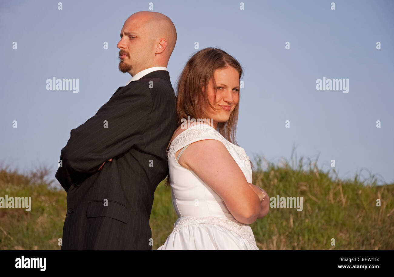 This young Caucasian bridge and groom have their backs towards one another in an argument. Shot outdoors with blue sky. Stock Photo