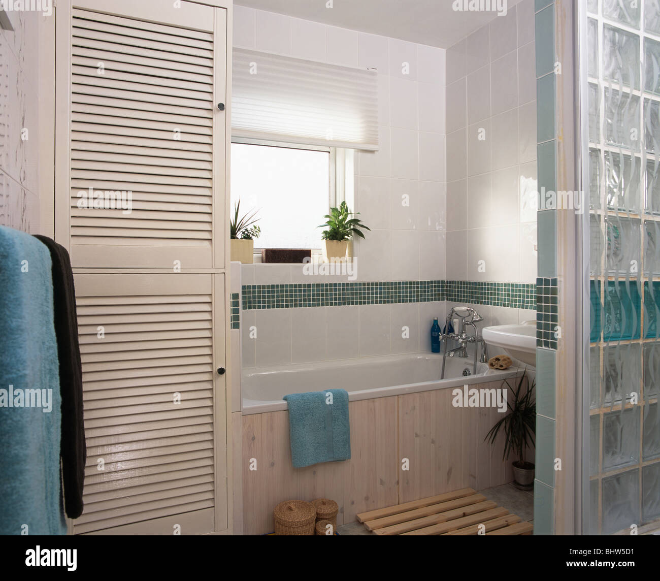 Louvre doors on storage cupboard in modern tiled bathroom with glass