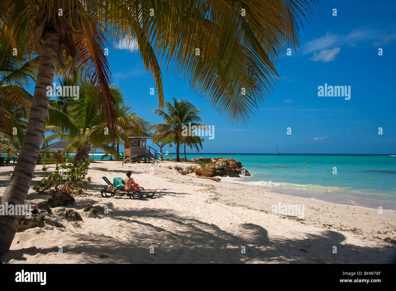 Pigeon Point Park beach Tobago with Caribbean sea coastline fringed with palm trees lifeguard point  seated bikini clad woman Stock Photo