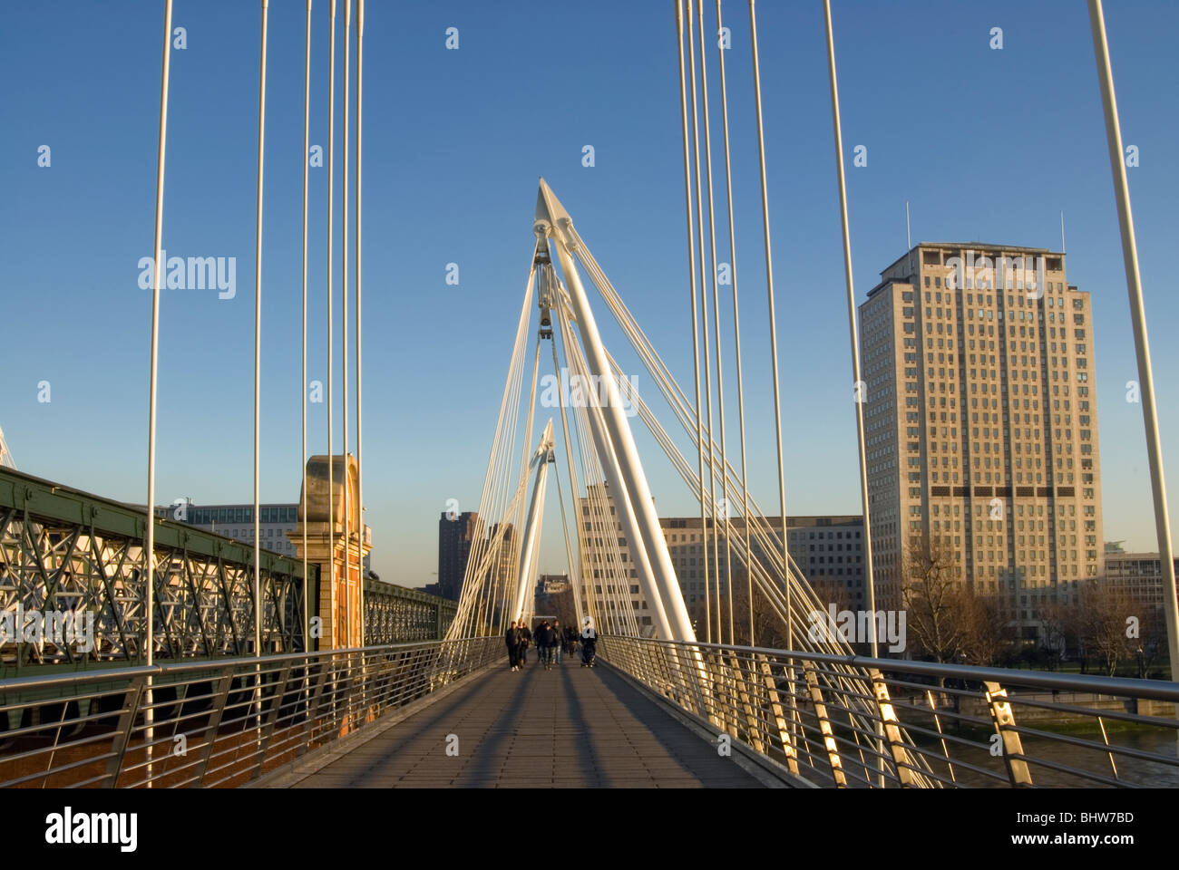 People walking along the Golden Jubilee Bridge in central London with the Shell building in the background. Stock Photo
