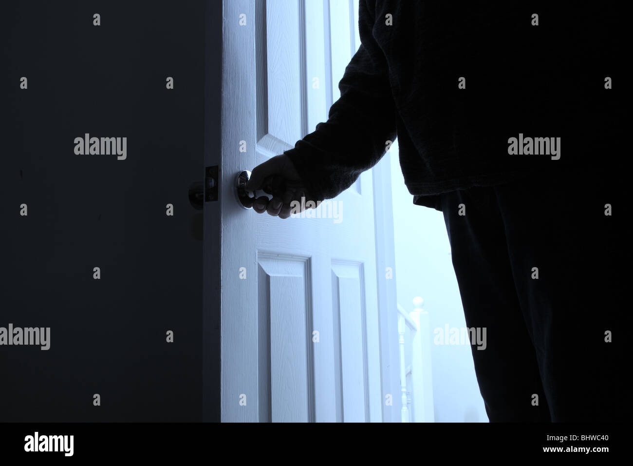 Man's hand turning the door handle, as he enters a dark room Stock Photo