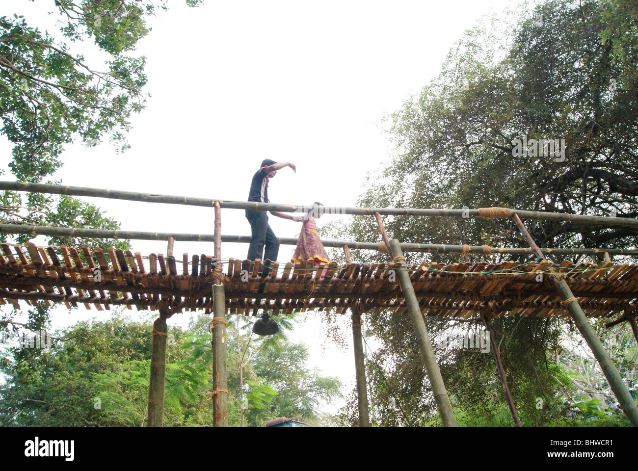 Brother helping small sister for Walking on the Top of Very narrow Bamboo Bridge.Bamboo Bridge Scene from Kerala,India Stock Photo