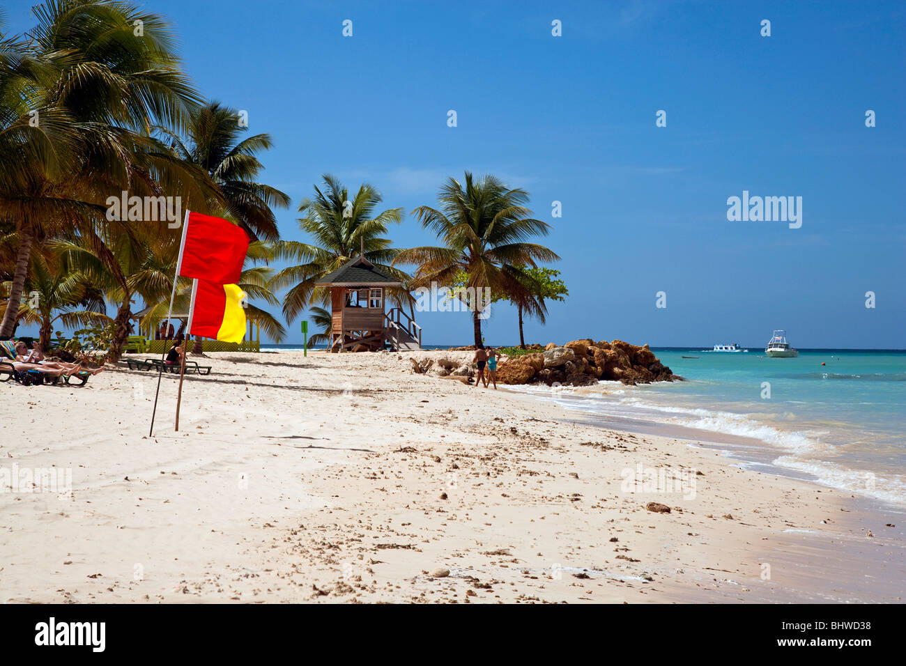 The beach at Pigeon Point Tobago with blue sky tropical sun with red and yellow lifeguard flags on display. Stock Photo