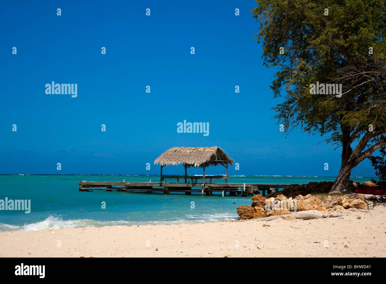 The thatched roof jetty at Pigeon Point Heritage Park Tobago against a blue sky and aquamarine sea. Stock Photo