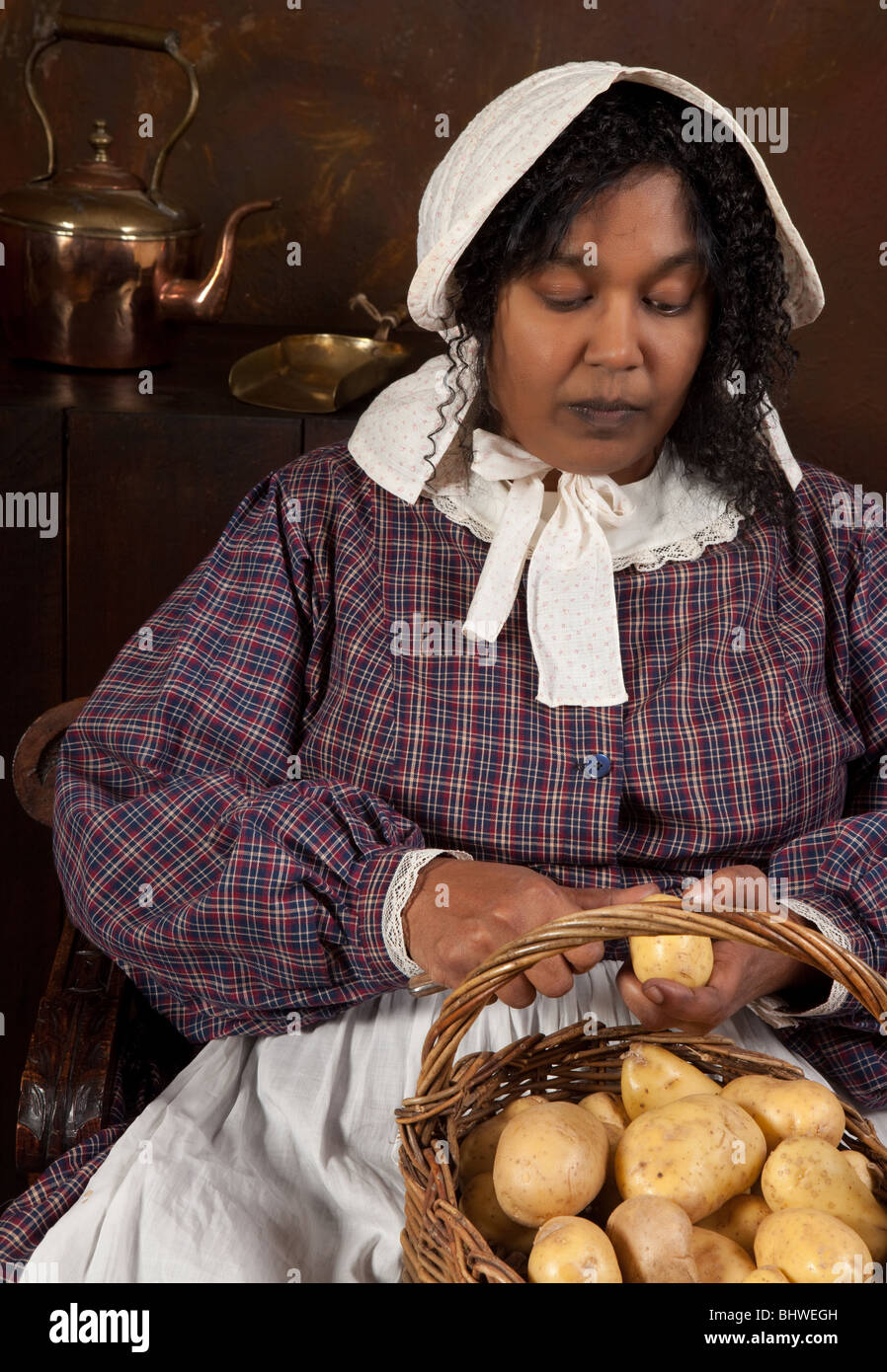 Reenactment scene of a black victorian maid peeling potatoes in an antique kitchen Stock Photo