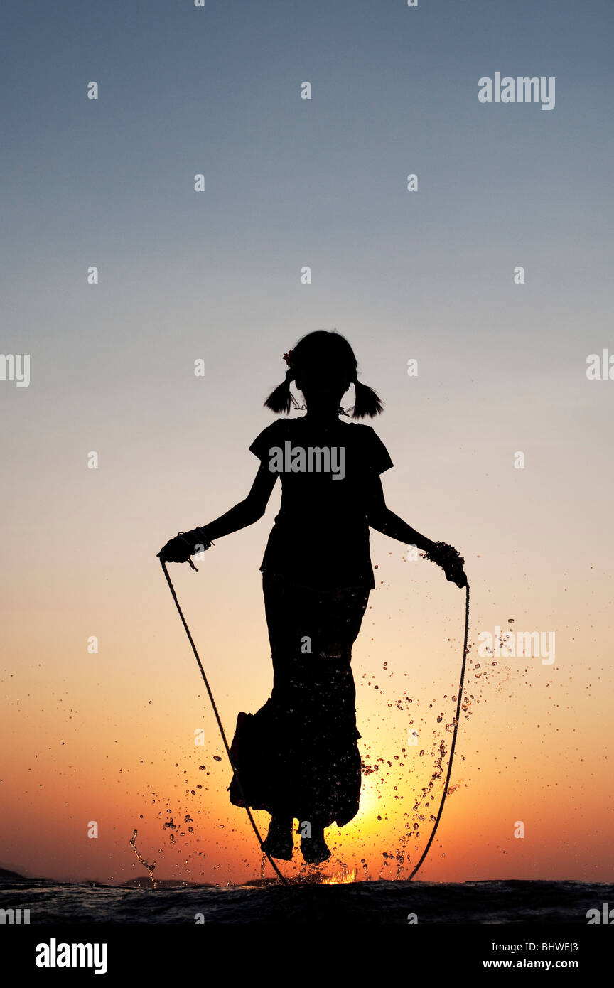 Silhouette of a young Indian girl skipping in water at sunset. India Stock Photo