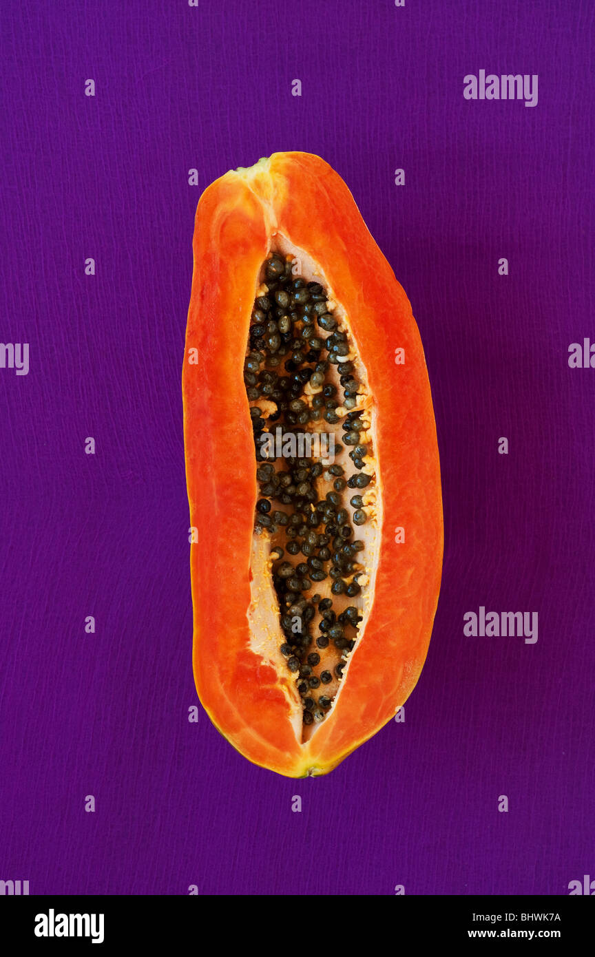 Cut papaya with seeds against purple background Stock Photo