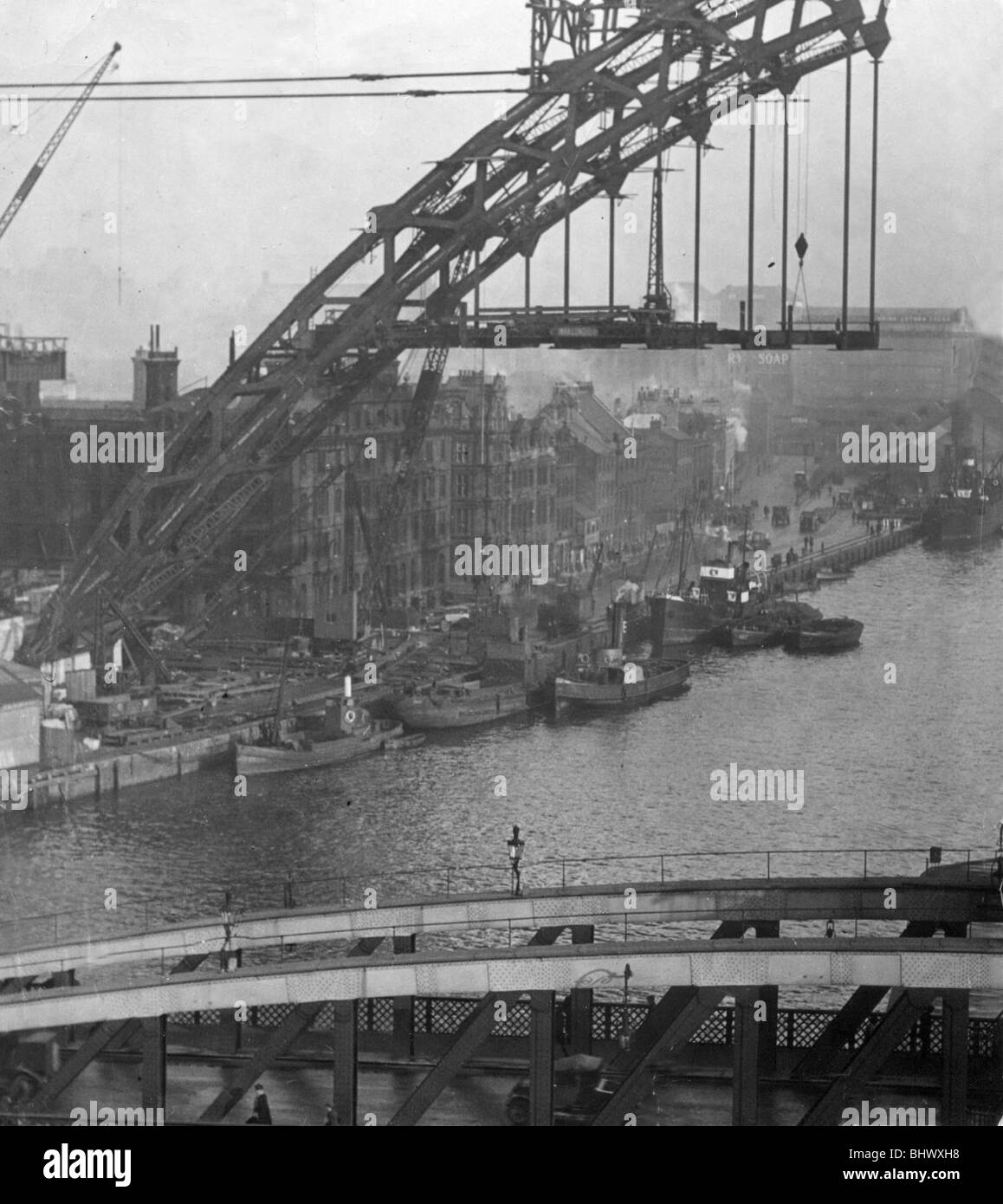 Fishing boats tied to the quay are frame by the Construction of Tyne Bridge in early 1928 The years of 1927 and 1928 were very special on Tyneside. Not only was the famous arched Tyne Bridge opened, pictured here under construction, but also the world-renowned Newcastle Brown Ale was launched. And not least Newcastle United lifted the Football League championship. Stock Photo